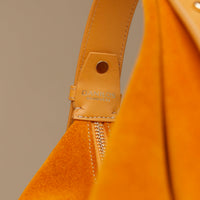 Close-up of a tan leather bag with 'Danilos' label on a beige background