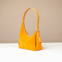 Yellow handbag with a beige strap on a white surface and beige background