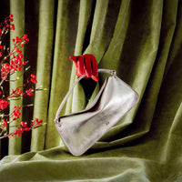 Silver handbag with red handle on a green fabric background