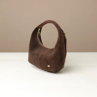 Brown suede leather danilos  handbag on a white surface with a beige background