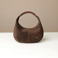 Brown suede leather danilos handbag on a white surface with a beige background