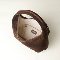 upper view of a opened Brown suede leather danilos  handbag with gold zipper on a light beige background
