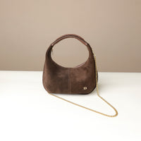 Brown suede leather danilos handbag with a gold chain on a white surface and beige background