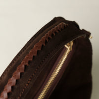Close-up of a brown leather danilos  bags handle with braided edge and gold zipper on a light background