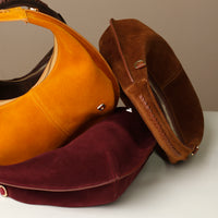 Three suede danilos handbags in brown, yellow, and red on a light gray surface.