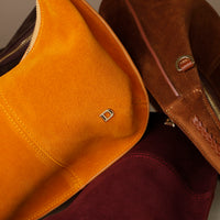 Close-up of a yellow and brown suede leather danilos handbag with a gold clasp.