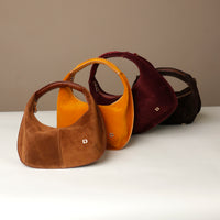 Four suede leather danilos handbag in brown, yellow and red on a white surface with a beige background.