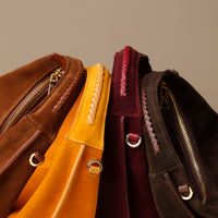 close up of Four suede leather danilos handbags handles in brown, yellow, red and dark brown on a beige background