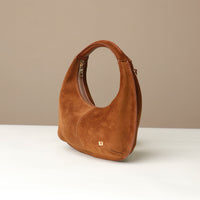 Brown suede leather danilos handbag on a white surface with a beige background