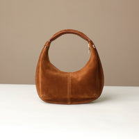 Brown suede leather danilos handbag on a white surface with a beige background