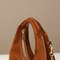 close up of a Brown round suede leather danilos handbag with gold zipper and chain detail on a neutral background