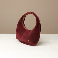 red burgundy rounded suede leather danilos handbag with gold zipper on a beige background