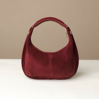 red rounded suede leather danilos handbag on a white surface with a beige background
