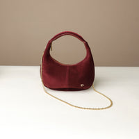 red rounded suede leather danilos handbag with a gold chain on a white surface and beige background