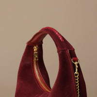 close up of a suede leather danilos handbag braid handle with gold zipper and chain detail on a beige background