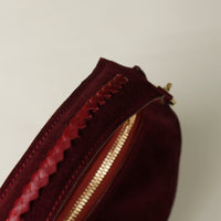 Close-up of a burgundy suede leather danilos handbag with a gold zipper on a beige background