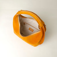 upper view of a opened Yellow suede leather danilos handbag with a visible brand logo on a light gray background
