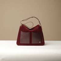 A Red suede shoulder bag with a square shape, featuring a structured design, an edge-cut, fold-over closure with a magnetic clasp, and a brand logo embossed on the bottom right.