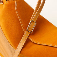 Close-up of a mustard yellow handbag with a strap and buckle on a white background