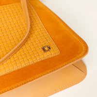 Close-up of a mustard yellow handbag with woven pattern and brand logo on a white background
