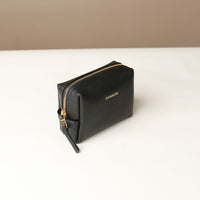 side view of a black Danilos leather toilet mini emma pouch with gold zipper on a beige background