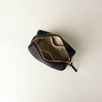 upper view of a open black Danilos leather toilet mini emma pouch with gold zipper on a beige background