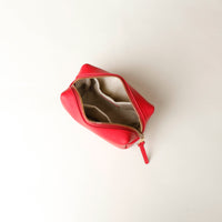 upper view of a open Red cosmetic bag mini emma danilos leather with organize pockets and zipper on a beige background