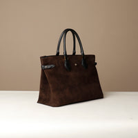 Brown leather handbag with black handles on a beige background