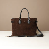 Brown leather handbag with black handle and strap on a beige background