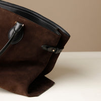 Close up view of Brown suede handbag with black handle on a beige background