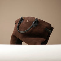 Brown suede handbag with black handle on a beige background