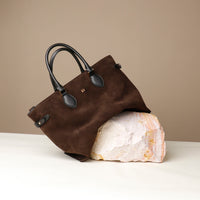 Brown suede handbag with black handle on a beige background on a rock