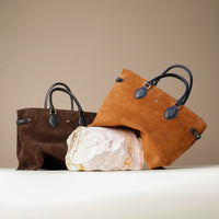 Two brown handbags with black handles and a large rock on a beige background