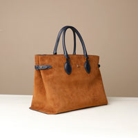 Brown suede handbag with black handle on a beige background