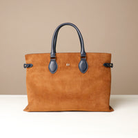 Brown suede handbag with black handle on a beige background