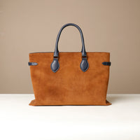 Brown leather tote bag with black handles and trim on a beige background