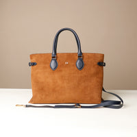 Brown leather tote bag with black handles and strap on a beige background