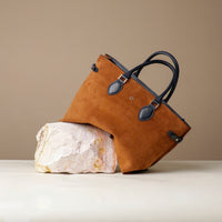 Brown leather bag with black handles on a beige background