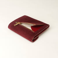 red suede leather danilos wallet with gold zipper on a light beige background