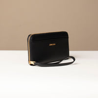 Side view of a black Danilos wallet Carlota with a visible handle drop and a gold zipper in a beige background
