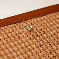 Close-up of a woven beige bag with a brown strap and gold buckle on a light background