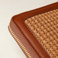 Close-up of a brown woven pouch with gold zipper on a light beige background