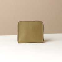 back view of a green zurich sr danilos leather wallet with gold zipper over a beige background