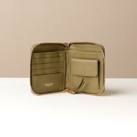 Front view of a open green zurich sr danilos leather wallet with gold zipper, card slots and two compartments over a beige background