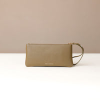 Green clutch bag on a white surface with a beige background