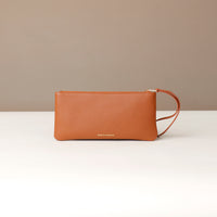 Brown leather clutch bag on a white surface with a beige background