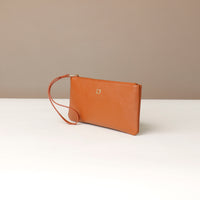 Brown leather clutch bag with a strap on a white surface and beige background